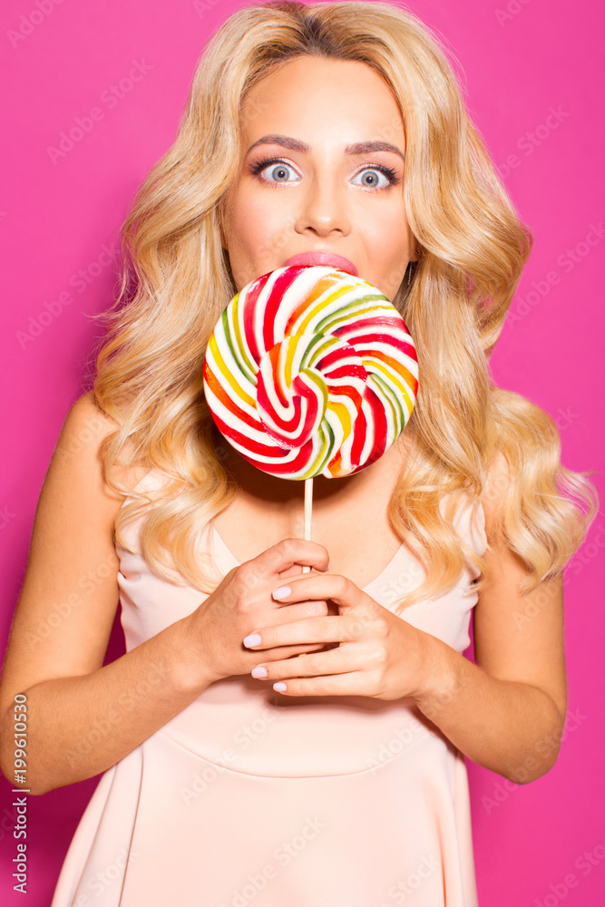 Beautiful girl with a big candy on a stick on a pink background