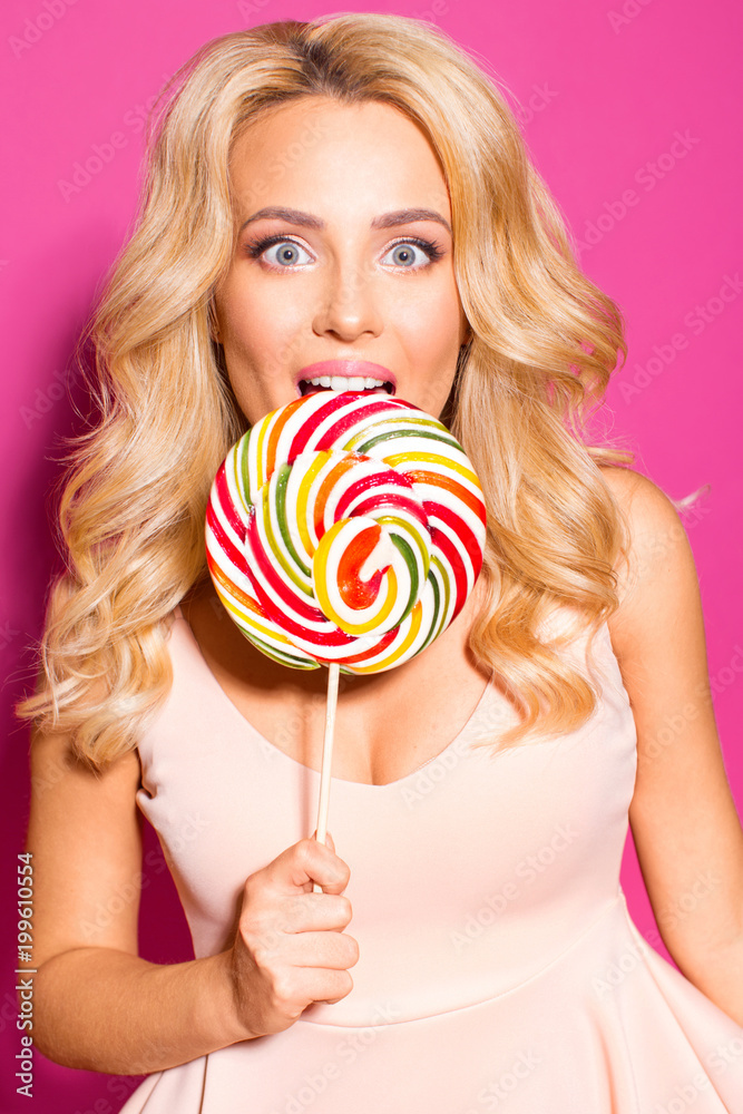 Beautiful girl with a big candy on a stick on a pink background