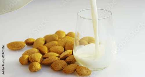 The almond milk is poured into a glass in slow motion, the background in woods there are almonds, perfect for a diet for a healthy diet and can be used as medicine. concept: diet, fitness, medicine.