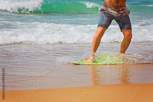 Young sportive man is running after his yellow and blue skimboard on the beach on a sunny day photo