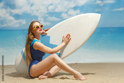 A girl with a surfboard in his hands on the sandy beach.
