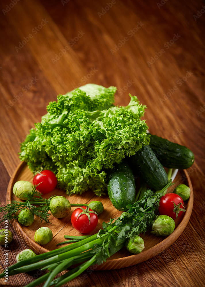 Vegetarian still life of fresh vegetables on wooden plate over rustic background, close-up, flat lay.