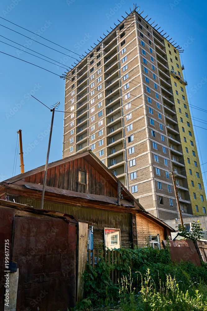 Old wooden house in front of a big tall modern skyscraper