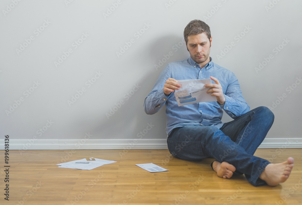 Handsome man sitting at the floor and looking at his bills. Handsome man sitting at the floor and looking at his bills.