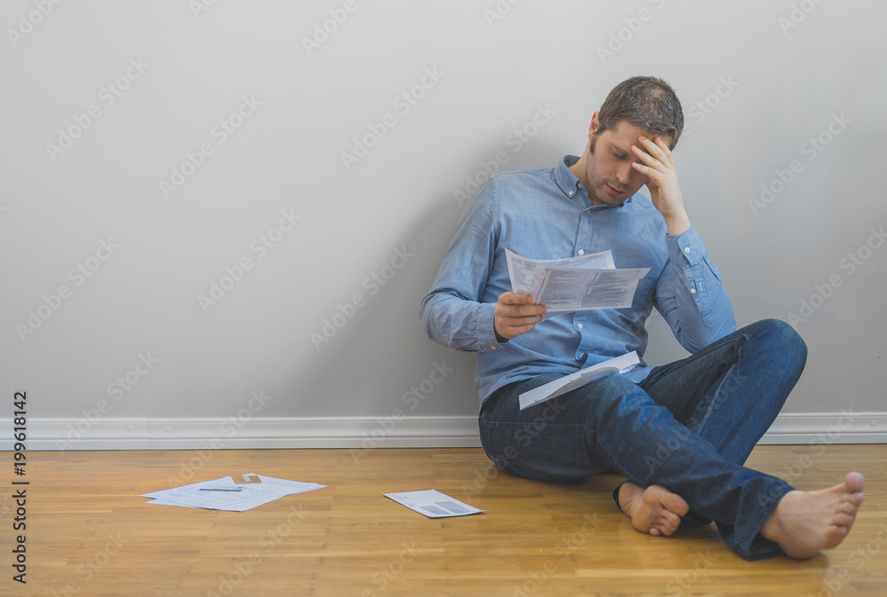 Sad man sitting at the floor and looking at his bills. Sad man sitting at the floor and looking at his bills.