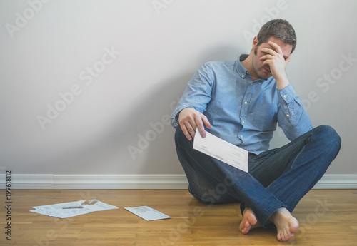 Very upset man sitting at the floor with bills.