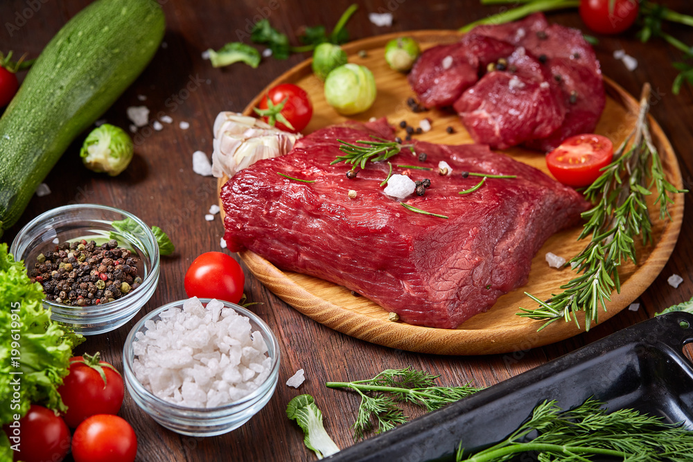 Flat lay of raw beefsteak with vegetables, herbs and spicies on metal tray, close-up, selective focus Flat lay of raw beefsteak with vegetables, herbs and spicies on metal tray, close-up, selective focus