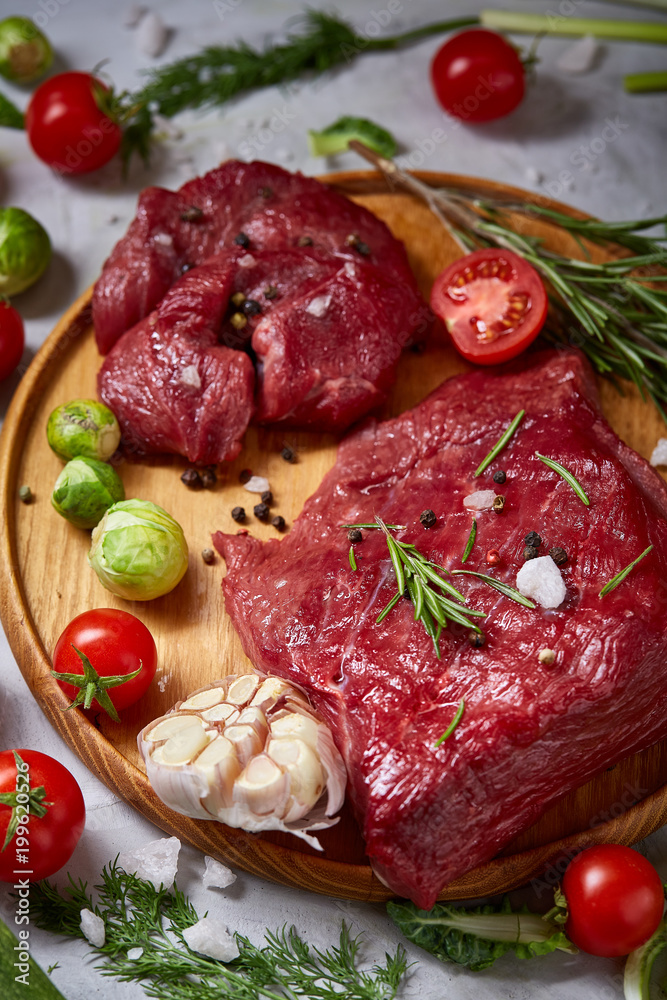 Still life of raw beef meat with vegetables on wooden plate over white background, top view, selective focus Still life of raw beef meat with vegetables on wooden plate over white background, top view, selective focus