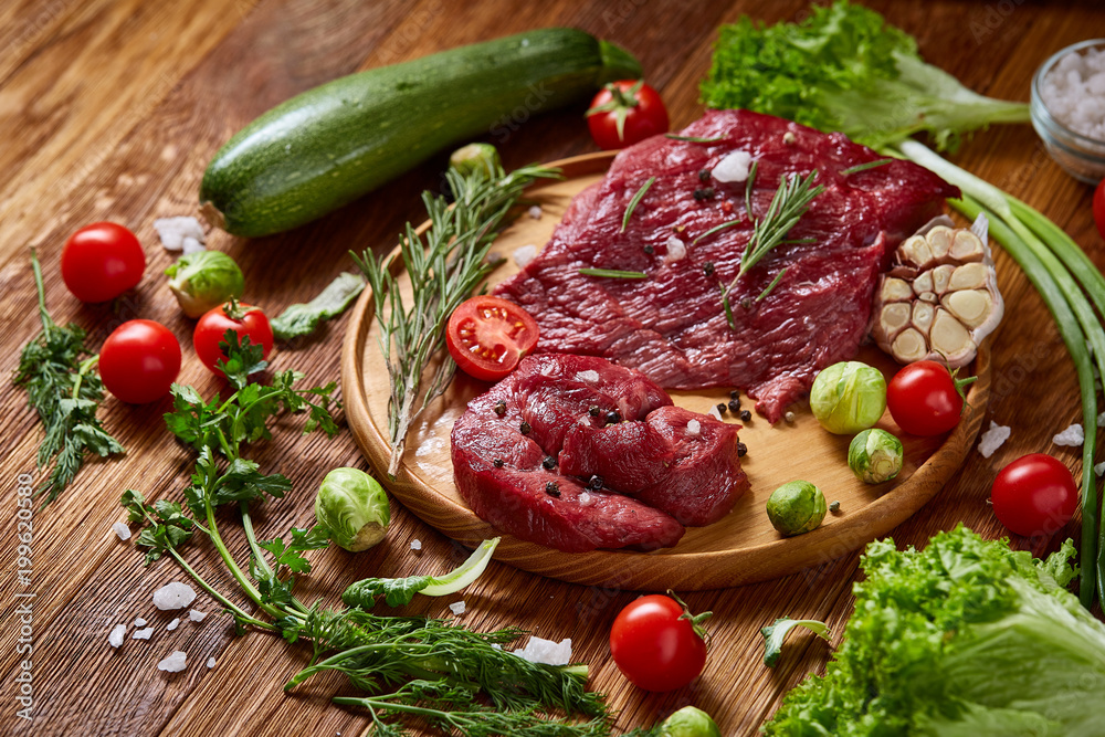 Still life of raw beef meat with vegetables on wooden plate over white background, top view, selective focus Still life of raw beef meat with vegetables on wooden plate over white background, top view, selective focus