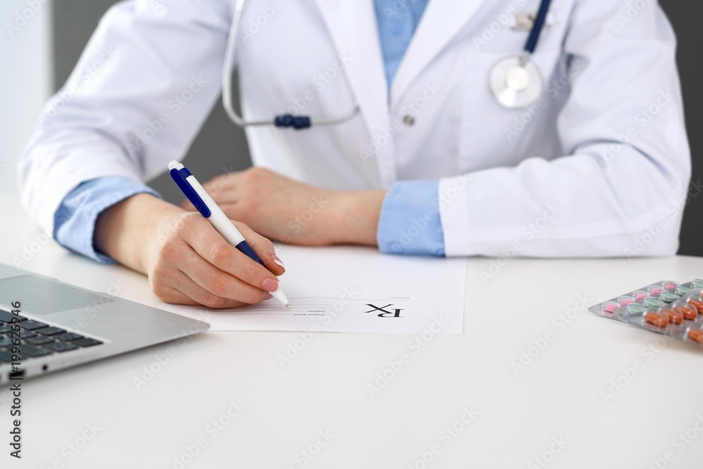 Female doctor filling up prescription form while sitting at the desk in hospital closeup. Healthcare, insurance and excellent service in medicine concept Female doctor filling up prescription form while sitting at the desk in hospital closeup. Healthcare, insurance and excellent service in medicine concept