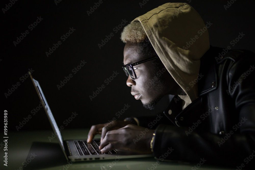 Handsome Afro American man using a laptop browse in internet till late at night. Afro man play games in darkness. Afro american hacker attack server in the night. Handsome Afro American man using a laptop browse in internet till late at night. Afro man play games in darkness. Afro american hacker attack server in the night.