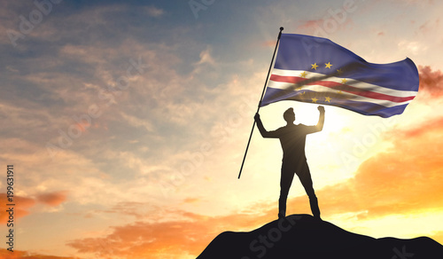 Cape Verde flag being waved by a man celebrating success at the top of a mountain. 3D Rendering
