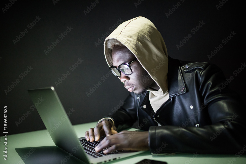 Afro american man sits at night at a computer desk using the Internet. Night surfing on the Internet. Gamer sits at night at a table near a computer with cookies in his hands and looks at the monitor Afro american man sits at night at a computer desk using the Internet. Night surfing on the Internet. Gamer sits at night at a table near a computer with cookies in his hands and looks at the monitor