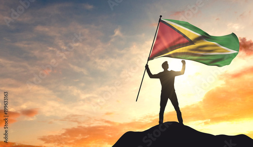Guyana flag being waved by a man celebrating success at the top of a mountain. 3D Rendering