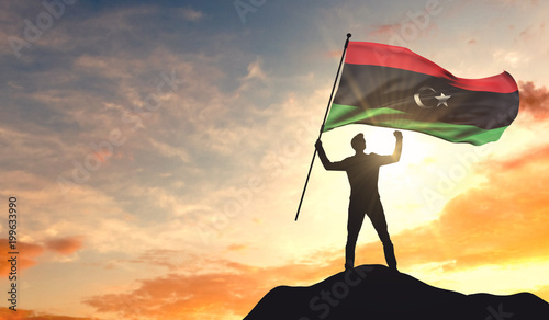 Libya flag being waved by a man celebrating success at the top of a mountain. 3D Rendering photo