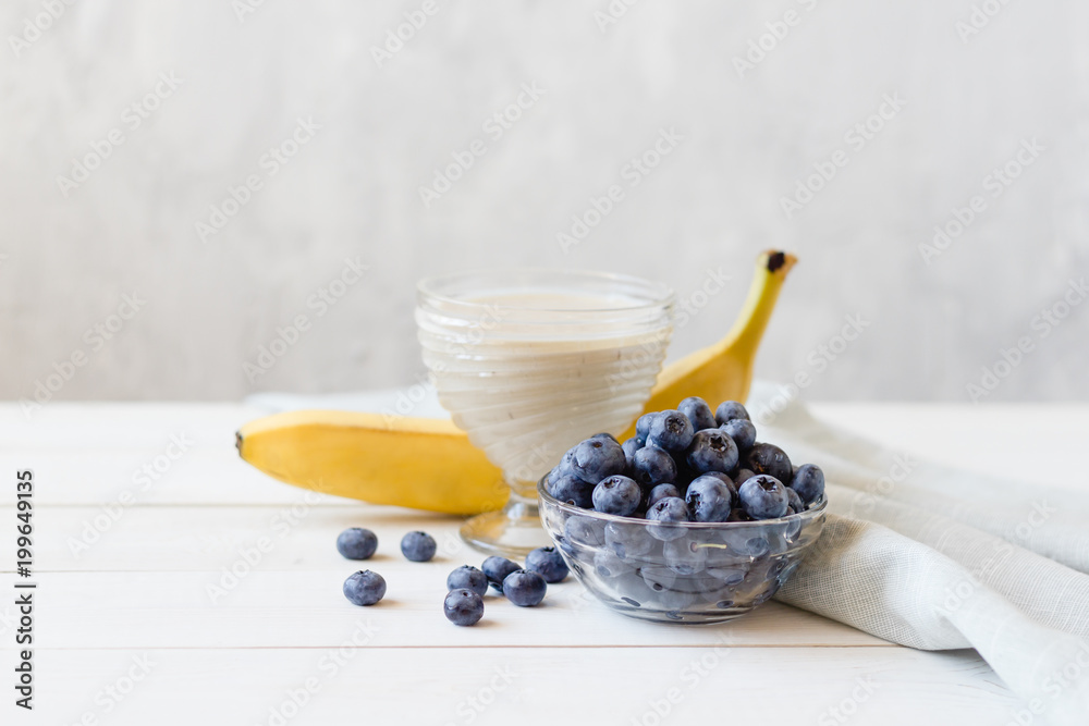 Banana smoothies and ripe blueberries in a glass bowl on a light background.