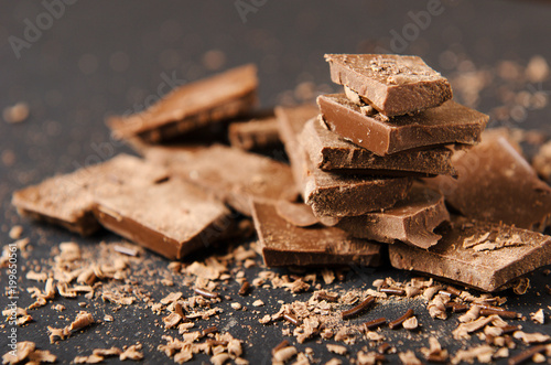Pieces of chocolate bar stacked with chocolate chips on a black background