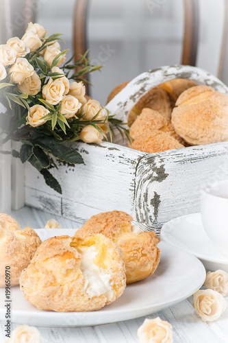 Many tasty cakes of Shue from custard paste with cream stuffing lie on a round plate on a white wooden table. photo