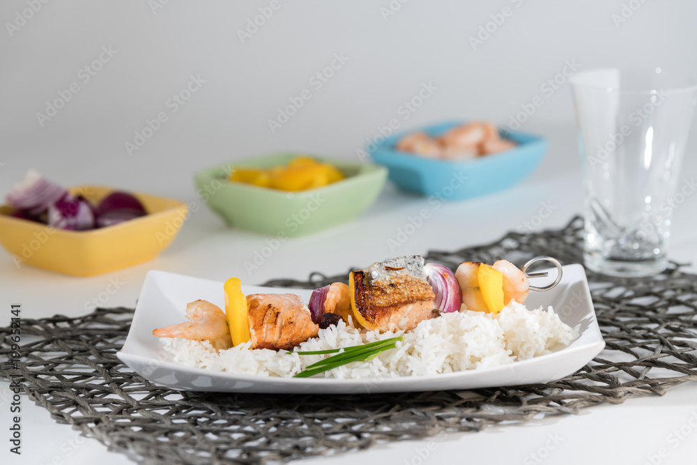Fischspieß angerichtet auf einem Teller mit Reis mit den Zutaten in Schälchen Fischspieß angerichtet auf einem Teller mit Reis mit den Zutaten in Schälchen