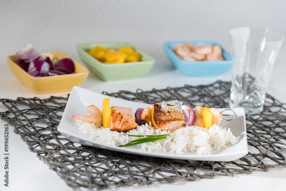 Fischspieß angerichtet auf einem Teller mit Reis mit den Zutaten in Schälchen Fischspieß angerichtet auf einem Teller mit Reis mit den Zutaten in Schälchen