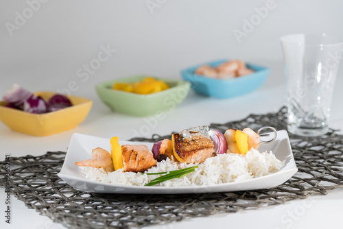 Fischspieß angerichtet auf einem Teller mit Reis mit den Zutaten in Schälchen