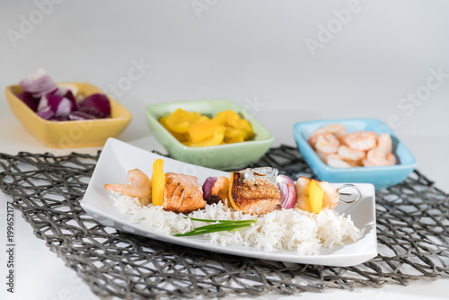 Fischspieß angerichtet auf einem Teller mit Reis mit den Zutaten in Schälchen