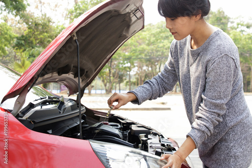 Young woman having a problem with her car. Repairing a car. Rechecks oil dipstick. Car check up in preparation for road trip. photo