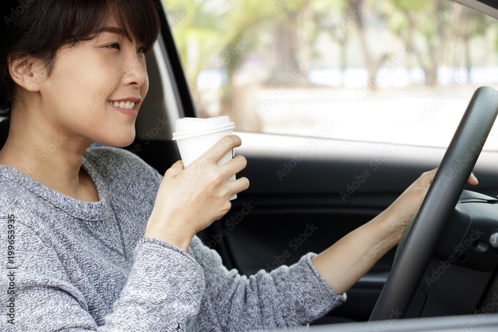 Young asian woman in casual wear driving a car and drinking coffee. Woman sitting in car with coffee. Business woman multitasking. Young asian woman in casual wear driving a car and drinking coffee. Woman sitting in car with coffee. Business woman multitasking.