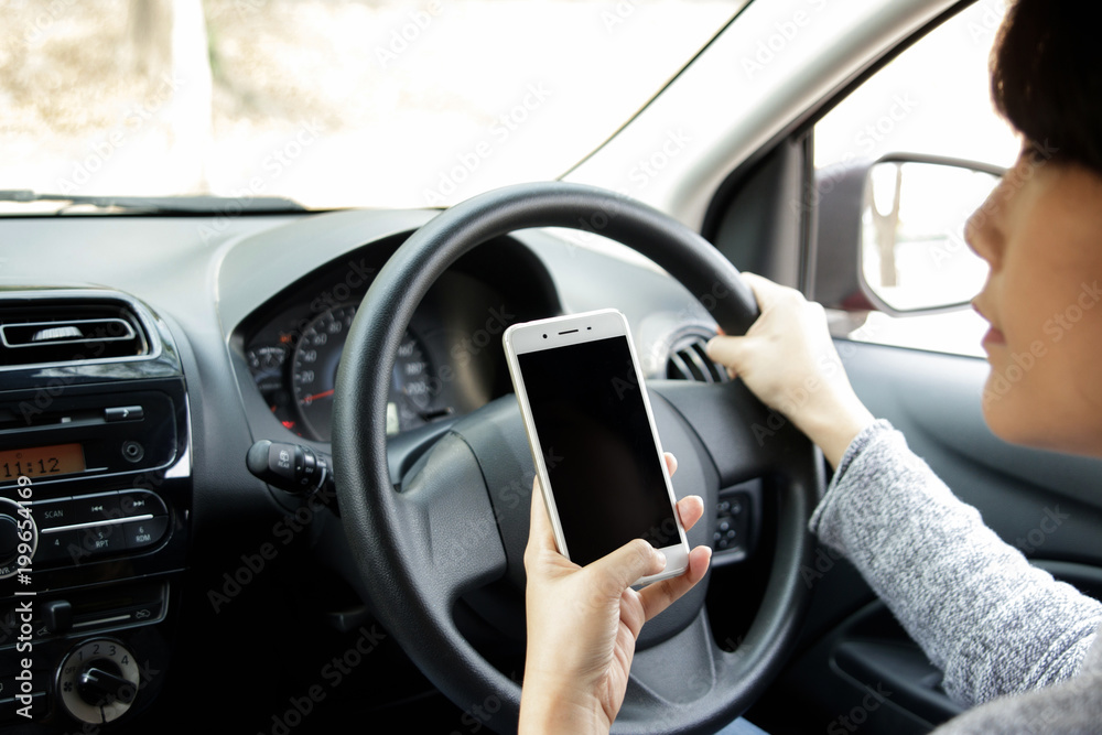 Young asian woman in casual wear driving a car and using smartphone. Back view.