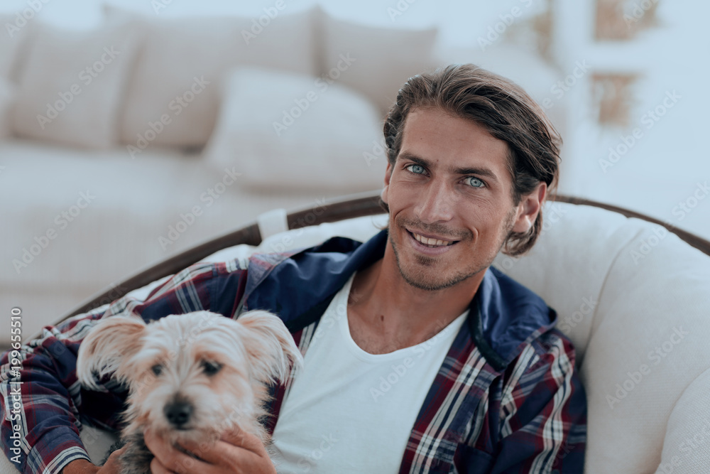 close-up of a smiling guy stroking his dog while sitting in a large armchair. close-up of a smiling guy stroking his dog while sitting in a large armchair.
