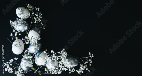 Diverse Group of silver Easter eggs with white flowers on black background, copy space, stylish original idea, selective focus