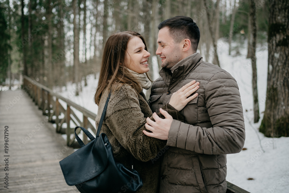 Fototapeta premium Stylish man with his attractive young wife smiling and embrace in the forest on the wooden bridge.