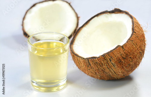 Coconut oil in a cup with split coconuts on a white background.