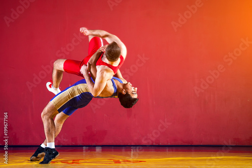 Fototapeta Naklejka Na Ścianę i Meble -  Two strong wrestlers in blue and red wrestling tights are wrestlng and making a  making a hip throw  on a yellow wrestling carpet in the gym. Young man doing grapple.