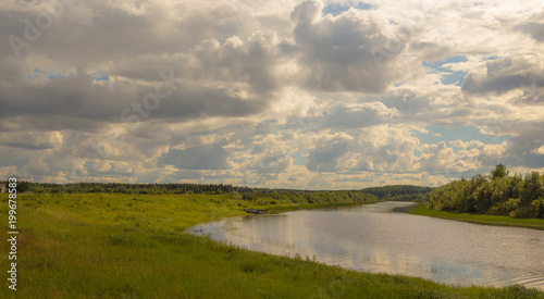A country view of a small river with banks covered with greenery and a beautiful sky with clouds