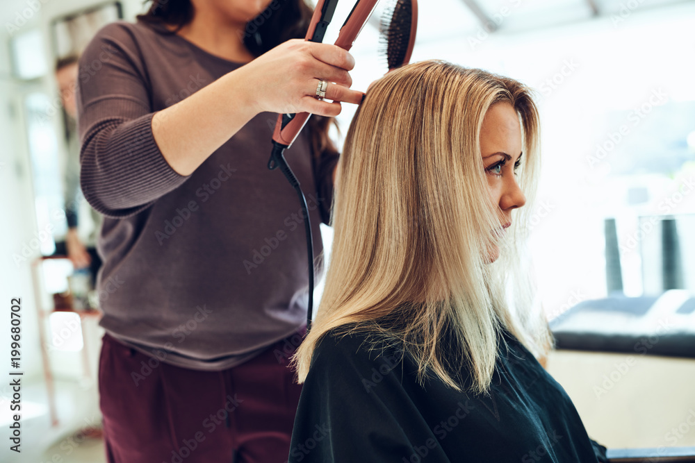Young woman getting her hair straightened at the salon Young woman getting her hair straightened at the salon