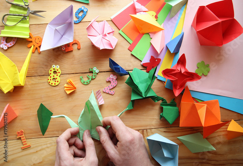 Man doing origami. Multicolored Origami and paper on  a wooden table.lesson of origami photo