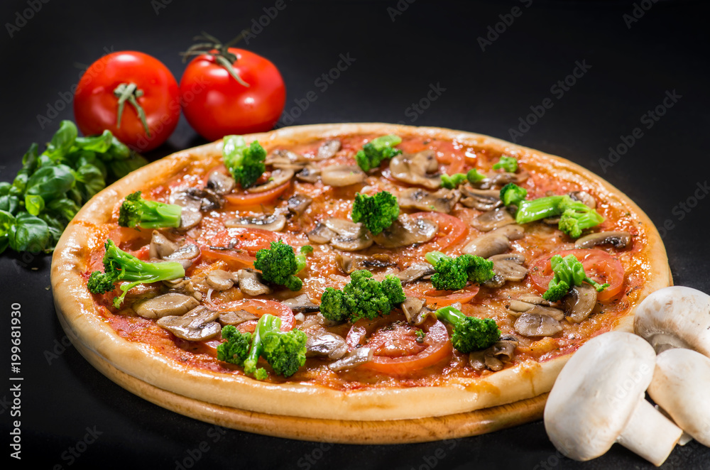 Pizza with mozzarella, mushroom, broccoli, onion and tomatoes on wooden board on dark background
