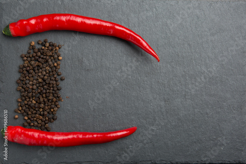 Hot red chili and black peper seeds on black background