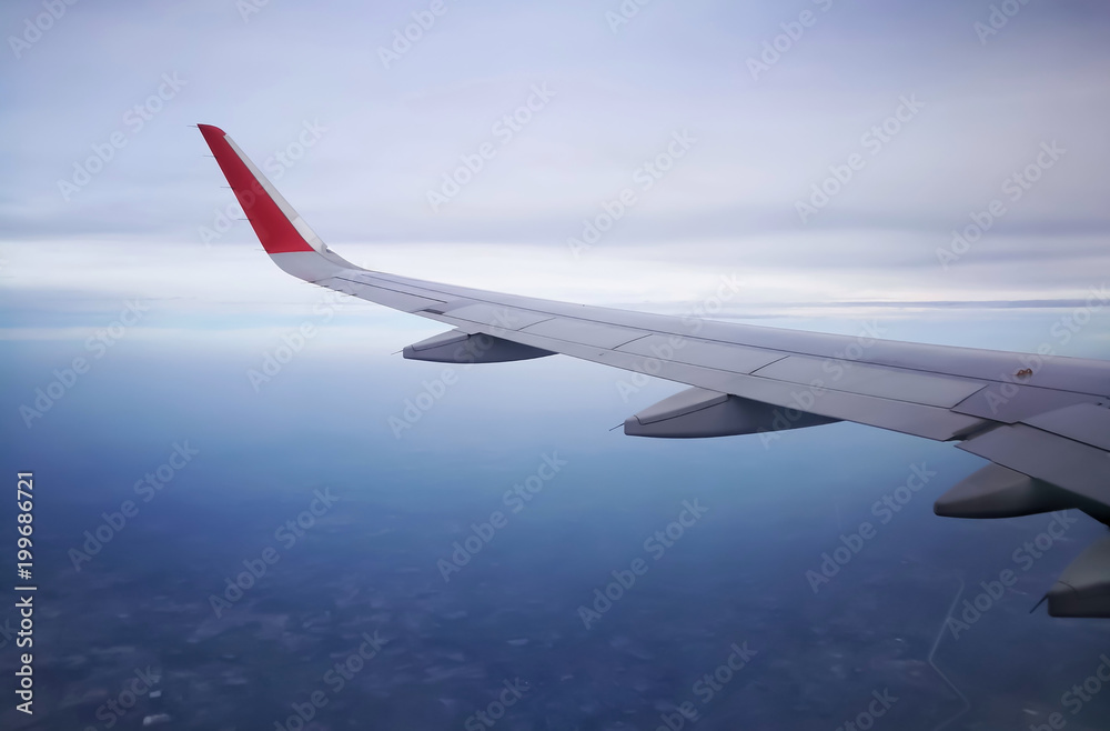 Fototapeta premium View from airplane. Beautiful plane wing; white clouds in the blue sky; blurred aerial view of city; taken through passenger window; copy space. Useful as visual contents for education, tourism, etc.
