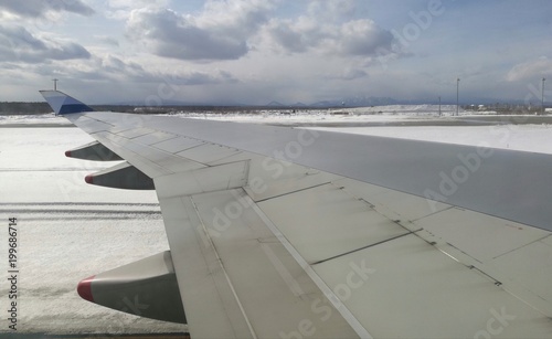 Airplane wing taken from plane window, moving on ground at an airport, mountain background, blue sky and snow covering in whole area. Useful as visual content for technology, education, tourism, etc.