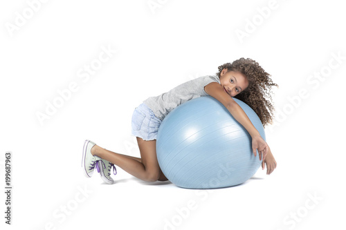 Young playful child or Pre teen biracial girl with brown curly hair playing or exercising on a large rubber ball