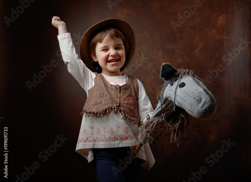 Slika na platnu Cute little girl dressed like a cowboy playing with a homemade horse