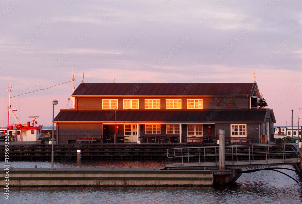 Laesoe / Denmark: The golden wintry twilight reflects in the windows of the public service building in the empty marina in Vesteroe Havn
