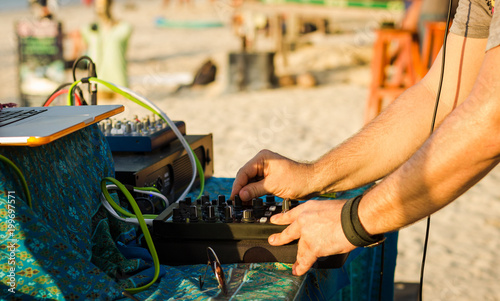 Close up on DJ playing music with professional equipment including console, laptop and power amplifier. Beach party at sunset in the island of Koh Phangan, Thailand