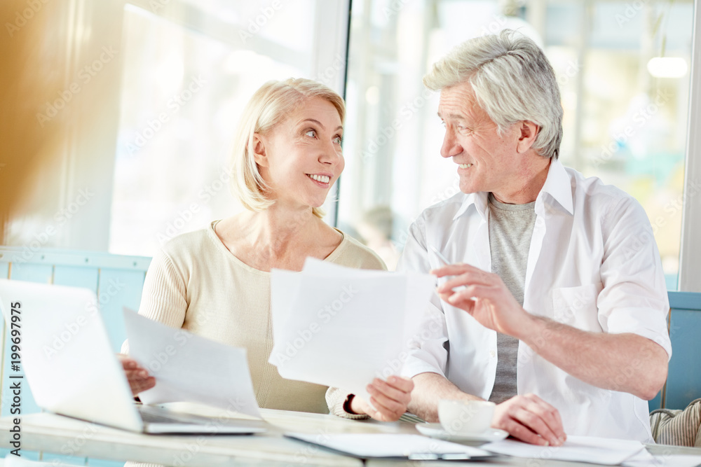 Professional brokers sitting in cafe and discussing new financial papers while preparing for meeting with partners Professional brokers sitting in cafe and discussing new financial papers while preparing for meeting with partners