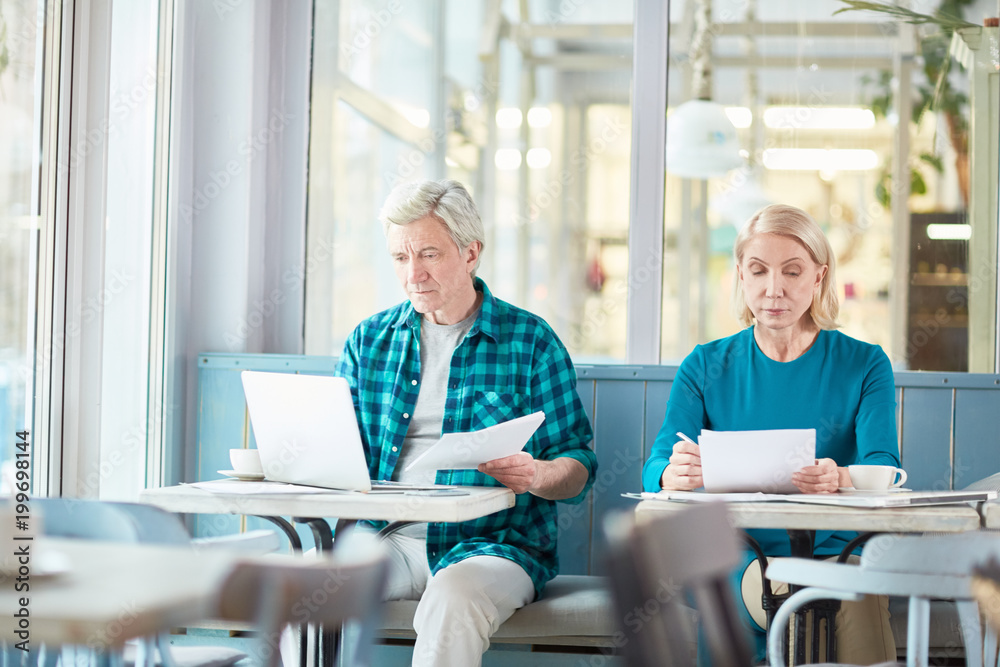Senior businessman with contract making changes in its text in laptop while his colleague checking data in financial papers near by Senior businessman with contract making changes in its text in laptop while his colleague checking data in financial papers near by