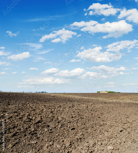 black plowed agriculture field and clouds in blue sky