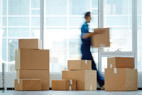 Blurred motion of contemporary worker with packed box walking to new office while delivering it to client