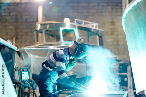 Engineer or welder in workwear carrying out his work in production department of shipbuilding factory